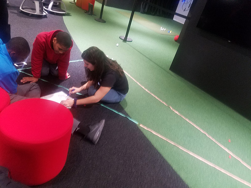 STEM Program Assistant Tiffani Kolozian helps Yohance Whyte, left, and Jason Johnson through a sample calculation.